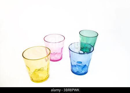 Four transparent plastic cups in yellow, pink, blue, and green arranged on a white background. Colourful drinkware with a modern, minimal look. Stock Photo