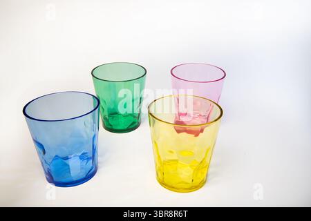 Four transparent plastic cups in yellow, pink, blue, and green arranged on a white background. Colourful drinkware with a modern, minimal look. Stock Photo