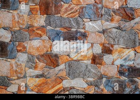 rustic stone wall featuring irregularly shaped stones in various shades of brown, gray, and beige. The stones are set in a random pattern, creating a Stock Photo