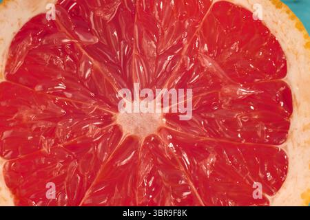 A bright, juicy grapefruit is sliced in half, showcasing its ruby red segments and shiny, textured surface Stock Photo