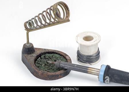 A soldering iron rests on stand beside spool of wire, showcasing essential tools for electronics work. setup is ideal for soldering tasks Stock Photo