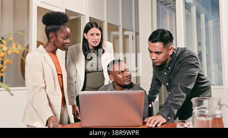 Diverse Team Collaborating Closely on a Project Using a Laptop in a Modern Office Setting Stock Photo