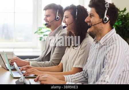 Smiling young call center operators in headsets providing customer support service in office. Stock Photo
