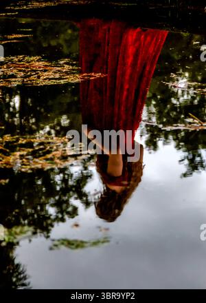 A person wearing a red dress is reflected in the water. Stock Photo