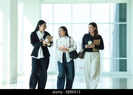 Happy Three Asian College Student Classmate walking on Campuss Hallway while Chatting and Discussing Stock Photo
