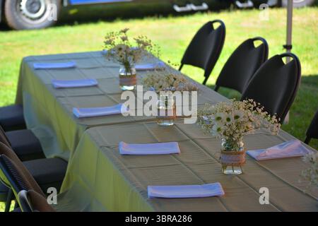 Outdoor rustic wedding reception table with white floral centerpieces and cloth napkins Stock Photo