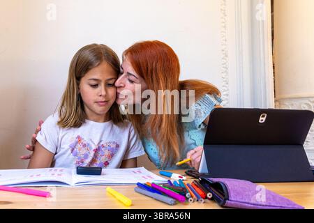 Mother kissing daughter while doing homework together at home Stock Photo
