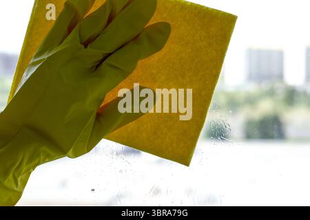A hand in a bright glove scrubs a window, making it shine in the daylight. Stock Photo