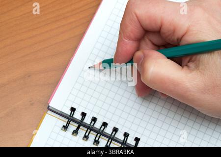 A person focuses on writing notes in a grid-patterned notebook. Stock Photo