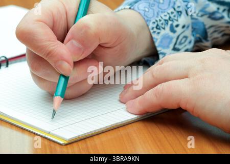 A person focuses intently while writing notes with a pencil on grid paper. Stock Photo