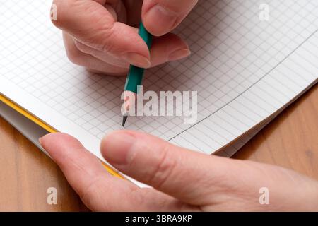 A hand skillfully writes on grid paper using a green pencil, capturing thoughts. Stock Photo