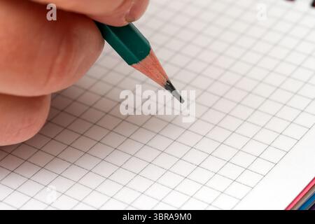 A hand gripping a green pencil prepares to jot ideas on squared paper. Stock Photo