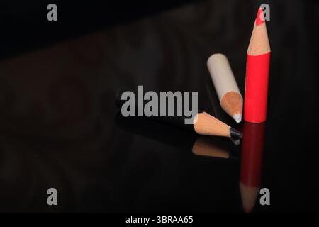 Three color pencils, red, black, and white, lie on a glossy surface, casting soft shadows. Stock Photo