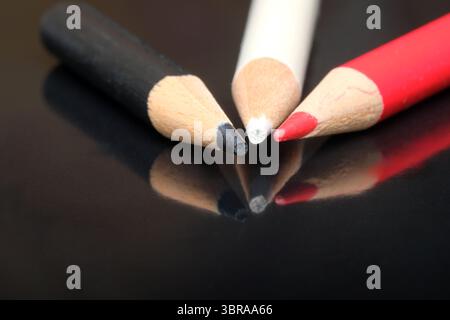 Three colored pencils lie on a glossy surface, highlighting their vibrant colors. Stock Photo