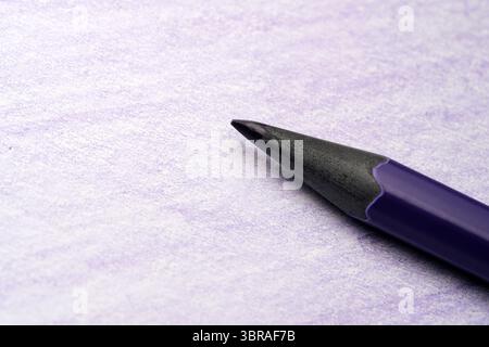 A colorful pencil rests on smooth purple paper, awaiting creativity. Stock Photo