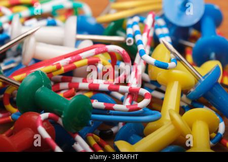 Colorful push pins and paper clips clutter a sunlit wooden desk. Stock Photo