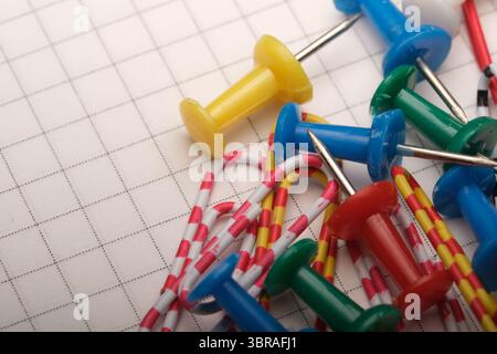 Brightly colored pushpins and paper clips are scattered across grid paper. Stock Photo