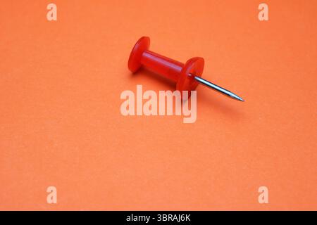 A red push pin stands out on a vivid orange surface. Stock Photo