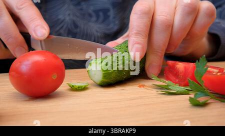 Hands slice cucumbers and tomatoes, preparing a fresh dish. Stock Photo