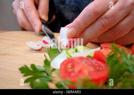 Hands skillfully slice radishes and cucumbers, preparing a fresh salad. Stock Photo