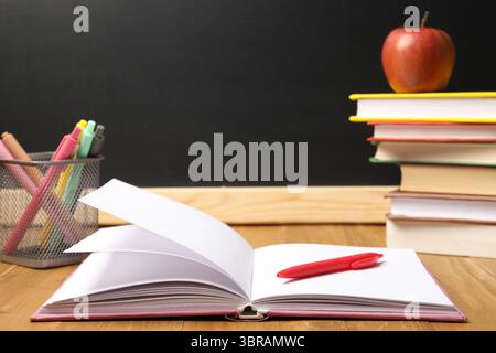 Different stationery and apple on wooden table near blackboard, closeup Stock Photo