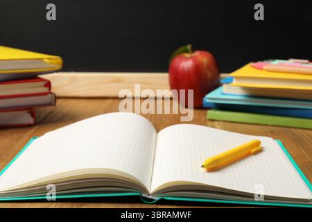 Different stationery and red apple on wooden table near blackboard, closeup Stock Photo