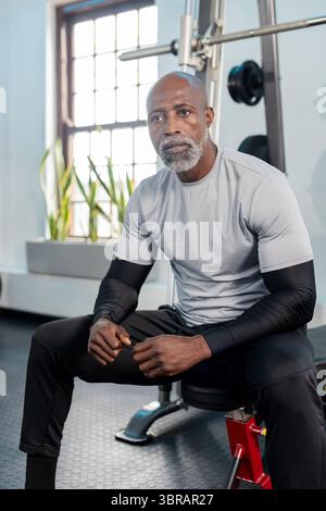 African American man sitting on bench press station in gym grasping barbell with weight plates Stock Photo