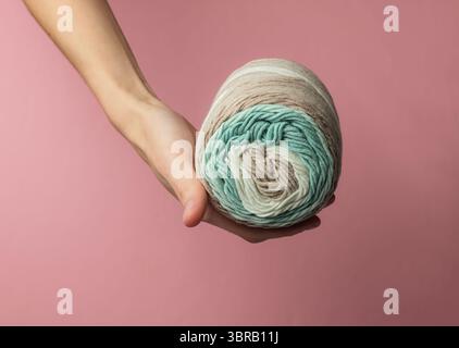 Female hand holds a skein of woolen threads on pink pastel studio background. Stock Photo