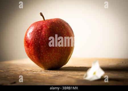 A vibrant red apple alongside a delicate white petal on weathered wood, illuminated by soft light, symbolizing freshness and subtle beauty. Stock Photo