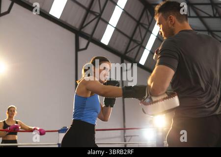 Boxing trainer with students practicing punches in gym ring with boxing gloves and focus mitts Stock Photo