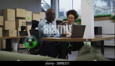 Collaborating colleagues presenting sustainability metrics on laptop in office, green icons Stock Photo
