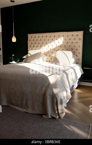 Master bedroom featuring tufted headboard with quilted duvet beside lamp and pendant light Stock Photo