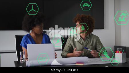 Two professionals discussing sustainability data icons and reviewing plans in conference room Stock Photo