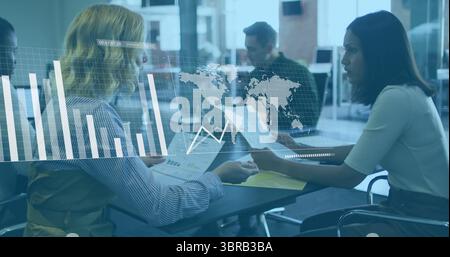 Discussing two women examining printed charts in open-plan office, with digital financial overlay Stock Photo