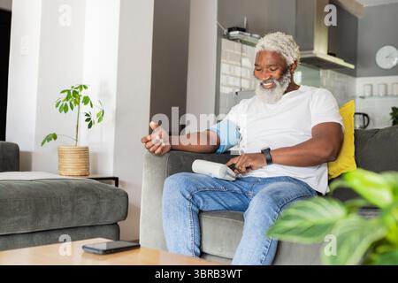 Senior African American man using blood pressure monitor while sitting on sofa at home, copy space Stock Photo