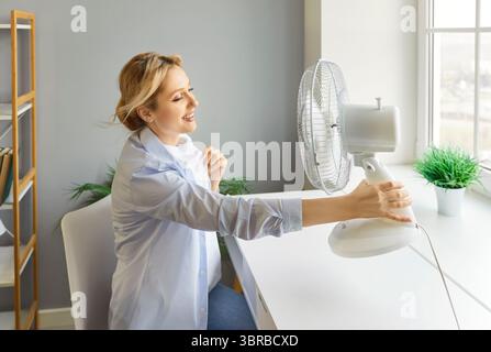 Woman enjoying freshness using electric ventilator, cooler to enjoy fresh air blowing from fan Stock Photo