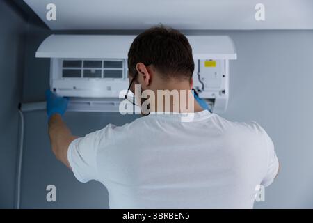 Skilled Technician Performing Maintenance on Air Conditioning Unit in Modern Interior Setting with Gray Walls and Minimalistic Design Stock Photo