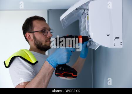 Professional technician, wearing gloves and glasses, carefully installing or repairing a wall-mounted air conditioning unit using a cordless Stock Photo