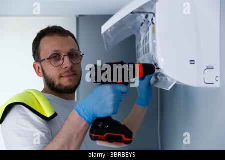 A skilled technician performs maintenance work on an air conditioning unit, using a power drill and wearing protective gloves to ensure safety during Stock Photo