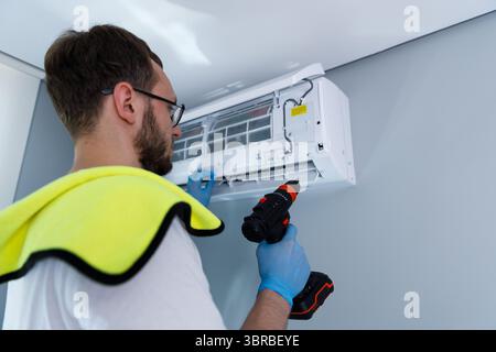 Professional technician performs routine maintenance on a modern air conditioning unit mounted on a wall, ensuring optimal performance in a Stock Photo