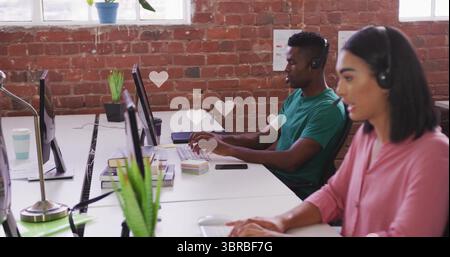 Middle Eastern woman in pink blouse in headset typing in office, monitors potted plants, copy space Stock Photo