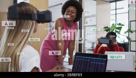 Collaborating colleagues testing VR headsets at conference table in office, with floating icons Stock Photo