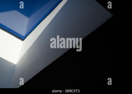 Triangular white ceiling forming skylight, framing blue sky through clear glass in vaulted hall Stock Photo