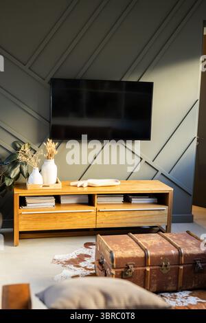 Flat-screen TV hanging on dark grey wall in living room corner, showcasing vases with dried grasses Stock Photo