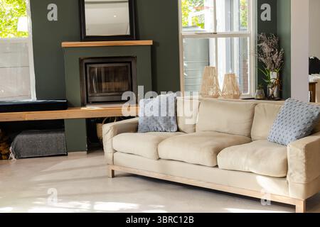 Featuring beige sofa with blue pillows against green wall and fireplace in living room Stock Photo