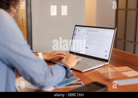 Non-binary professional in denim jacket working on proposal on laptop in home studio with swatches Stock Photo