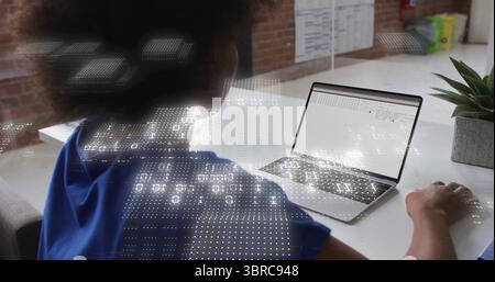 Typing woman wearing blue shirt analyzing laptop spreadsheet on office desk, with data overlays Stock Photo