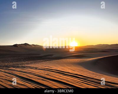 Sun going down behind sand dunes in desert  arid landscape scenery Huacachina, Ica, Peru. Tourist destination for extreme sports, buggy  adventure. Stock Photo