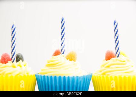 vector art showing three yellow-frosted cupcakes blue striped candles, gumdrops on white background Stock Photo