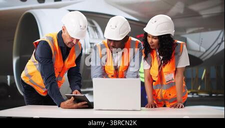 African American Supervisor Inspects Aircraft While Hispanic Technician Repairs Engine. Stock Photo